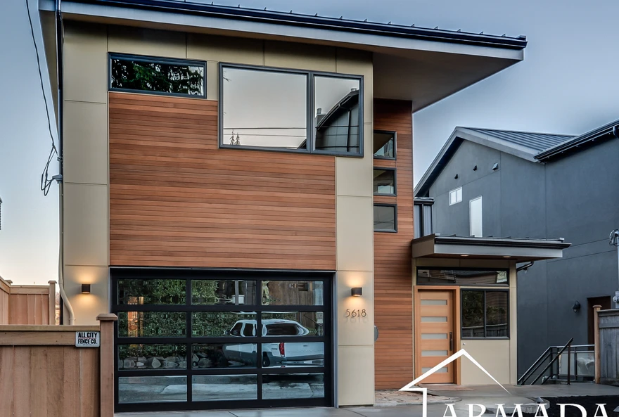 Modern two-story house with wood and beige exterior, large windows, and a glass-paneled garage door. The entryway is covered, and the house number 5618 is visible near the front door.
